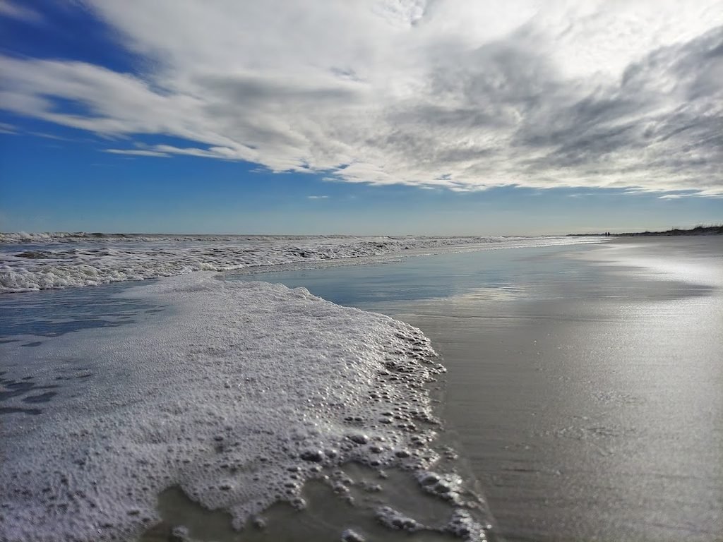 Ocean foam spreading across wet sand beneath dramatic clouds at Kiawah Island Beach, South Carolina.