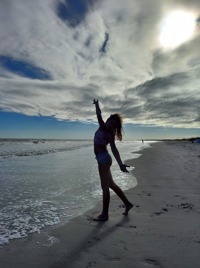 Girl posing at the shoreline beneath dramatic clouds at Beachwalker Park on Kiawah Island, South Carolina.